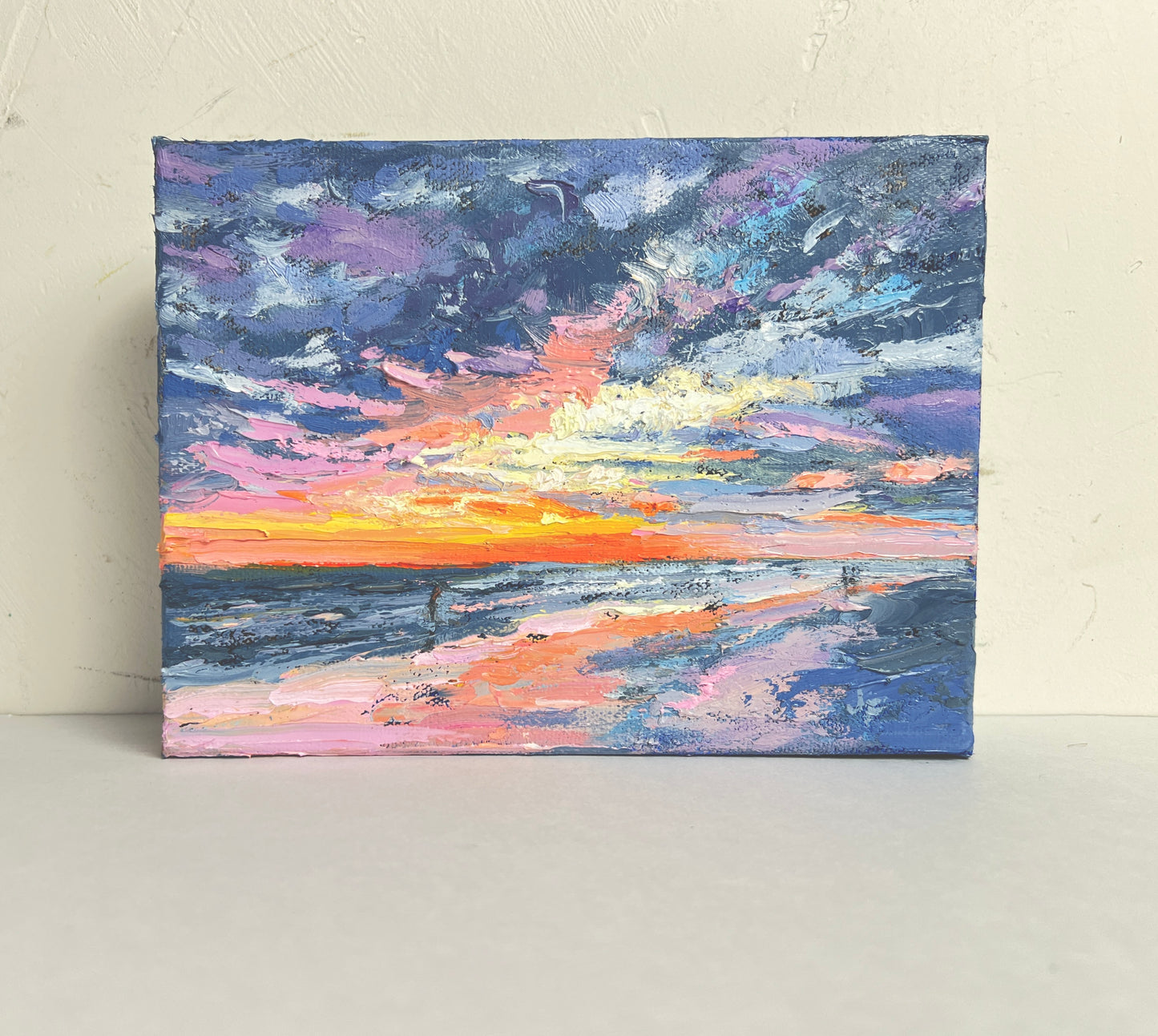 Painting of a sunset over water with a colorful sky.